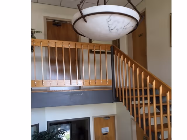 Interior lobby with a wooden staircase, second-floor balcony, and a large circular ceiling light.