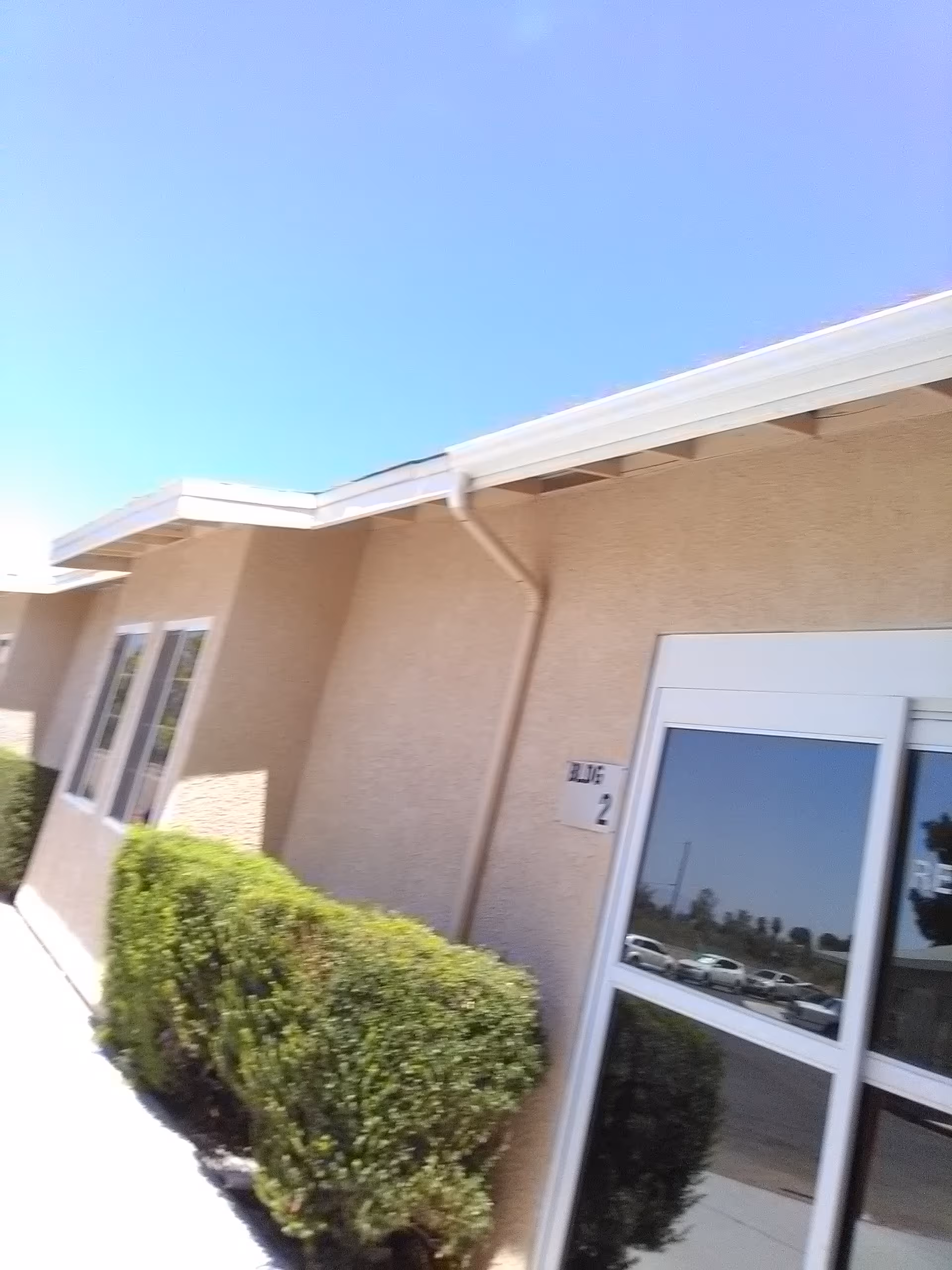 Beige senior living facility exterior with trimmed hedges and glass entrance doors.
