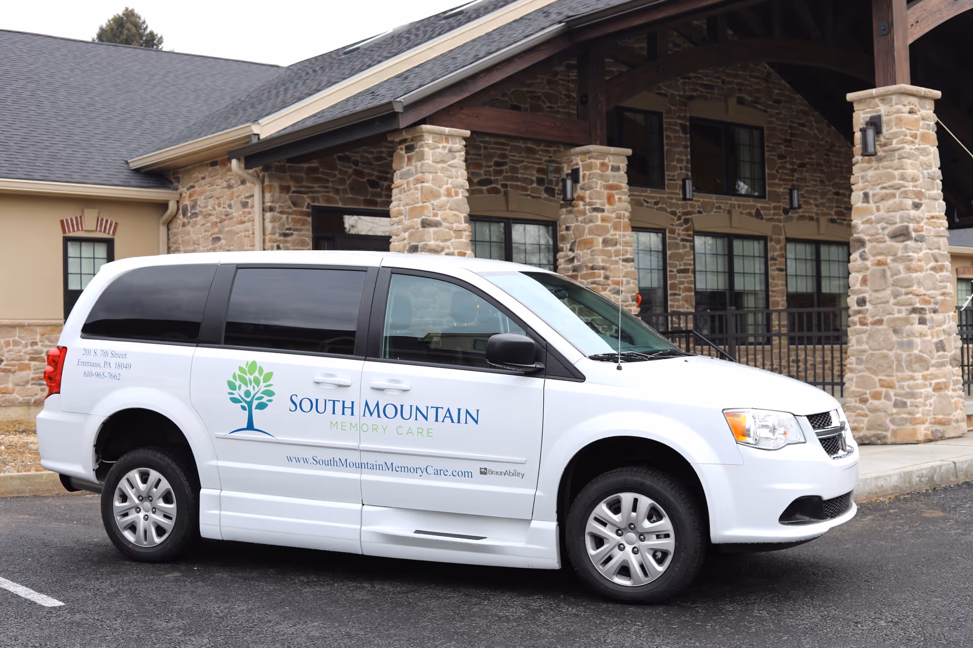 White van parked in front of a stone building with pillars. The van has the logo and text for South Mountain Memory Care on the side, including a tree graphic, address, phone number, and website.