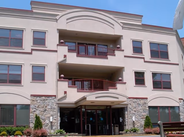 Three-story beige senior living building with arched entry, balconies and stone accents.