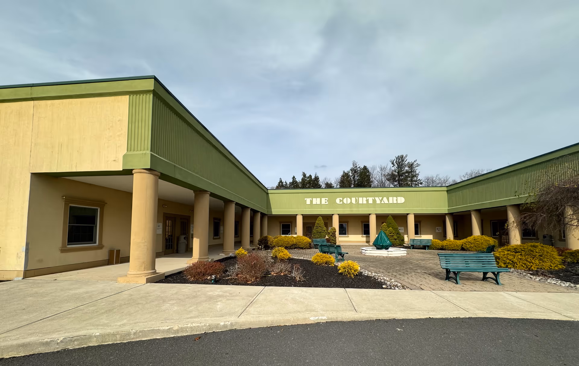 Exterior view of a single-story senior care facility courtyard with benches and a central fountain.