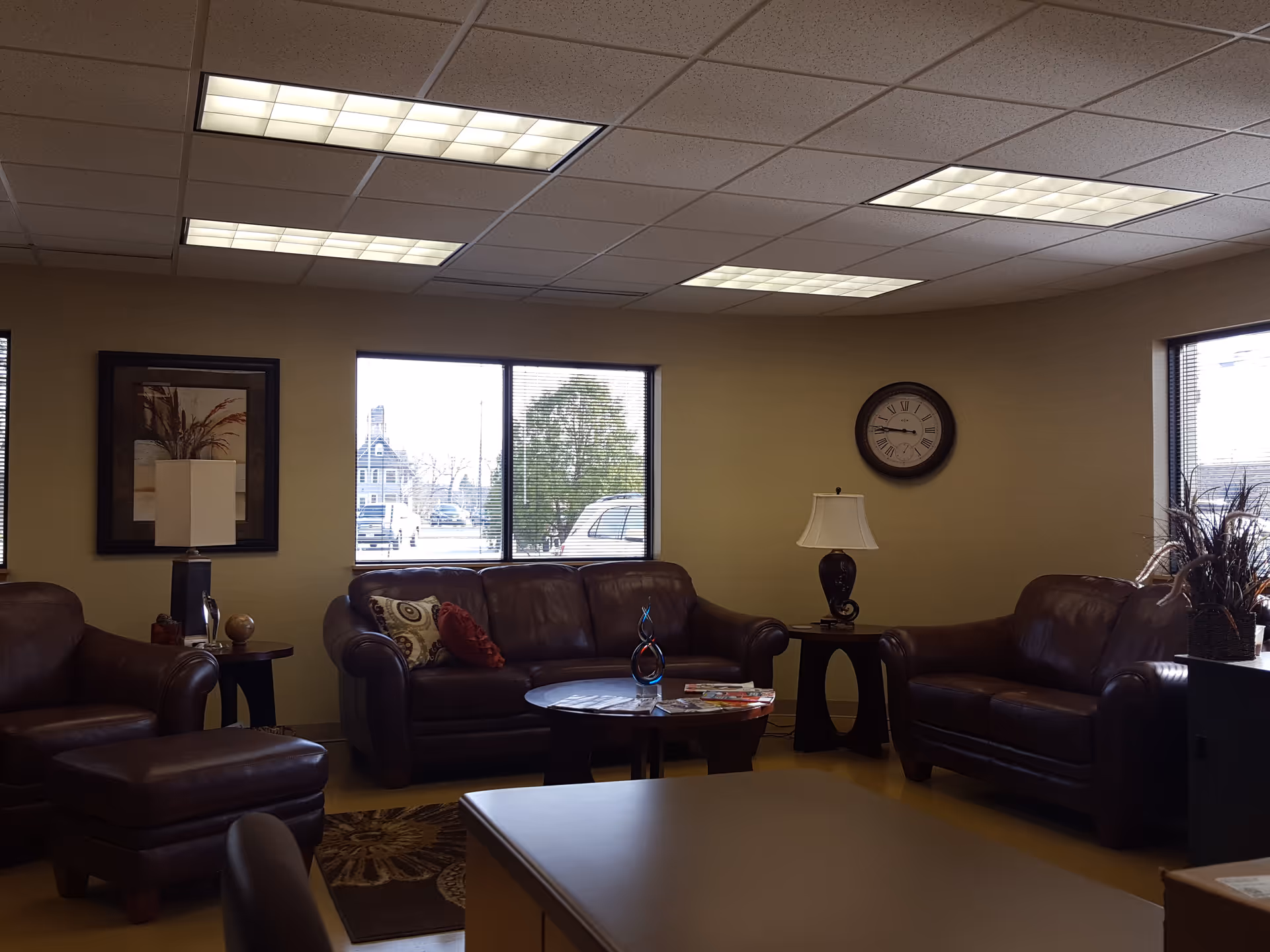 Cozy lounge area with brown leather sofas, coffee table, lamps, and windows in a senior residence.