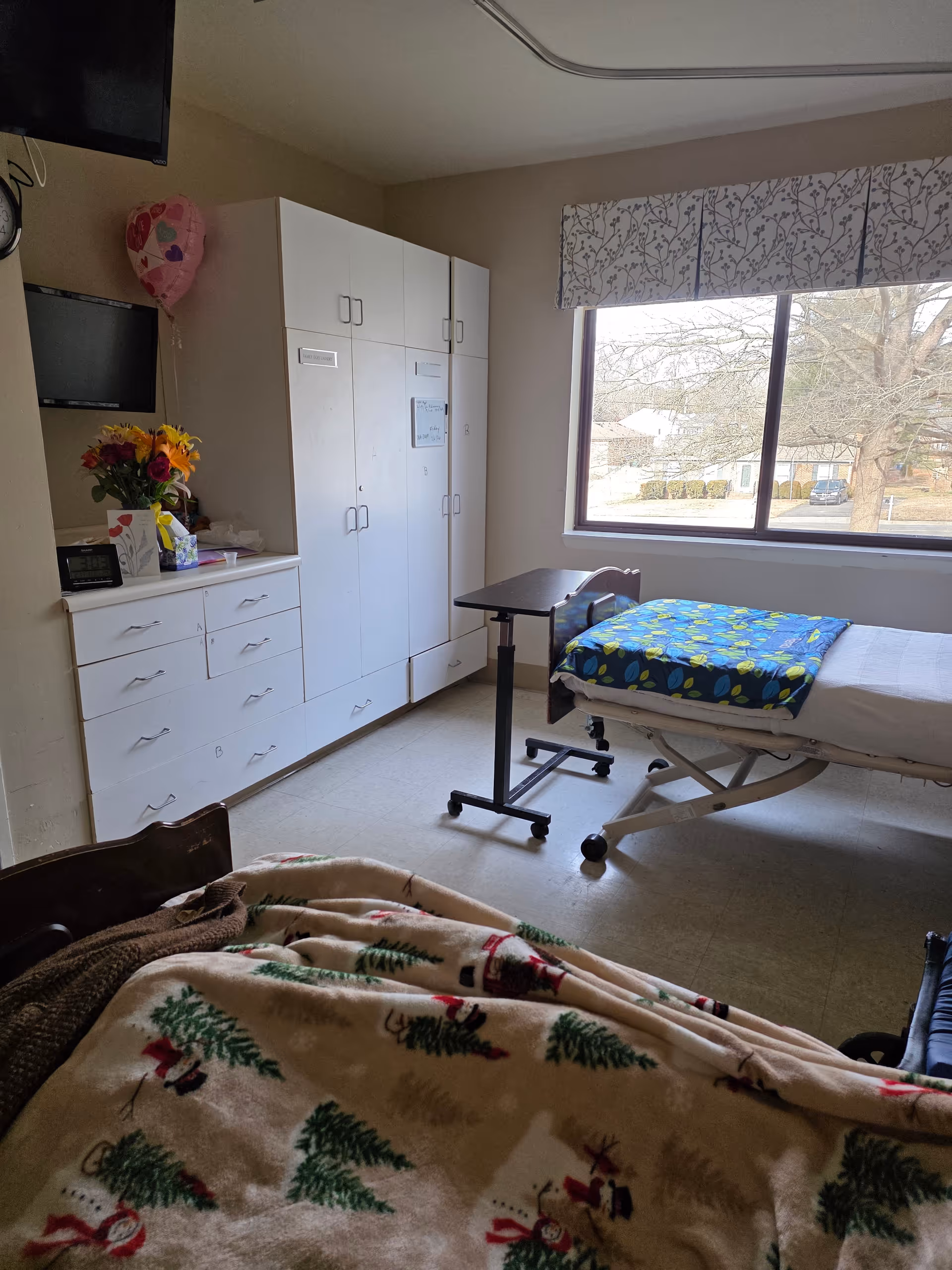 This is a furnished senior living bedroom with a bed, wardrobe, dresser, and window.