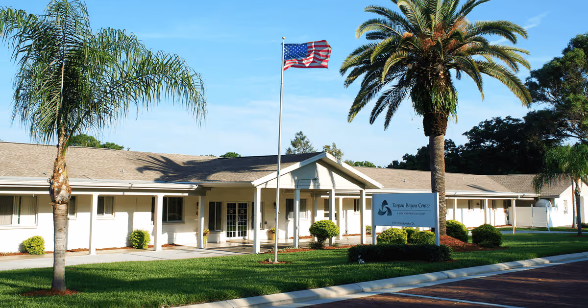Tarpon Bayou Center exterior: a single-story facility with palm trees, flag, and manicured lawn.