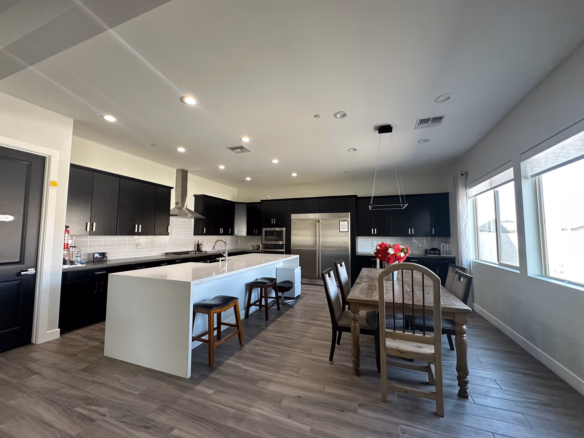 Bright, modern kitchen with black cabinets, stainless appliances, an island, and a dining table.