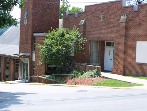 Exterior view of a brick facility entrance with greenery and a small landscaped area.