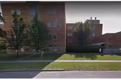 Exterior view of a brick senior living facility with trees, sidewalk, and grassy lawn.