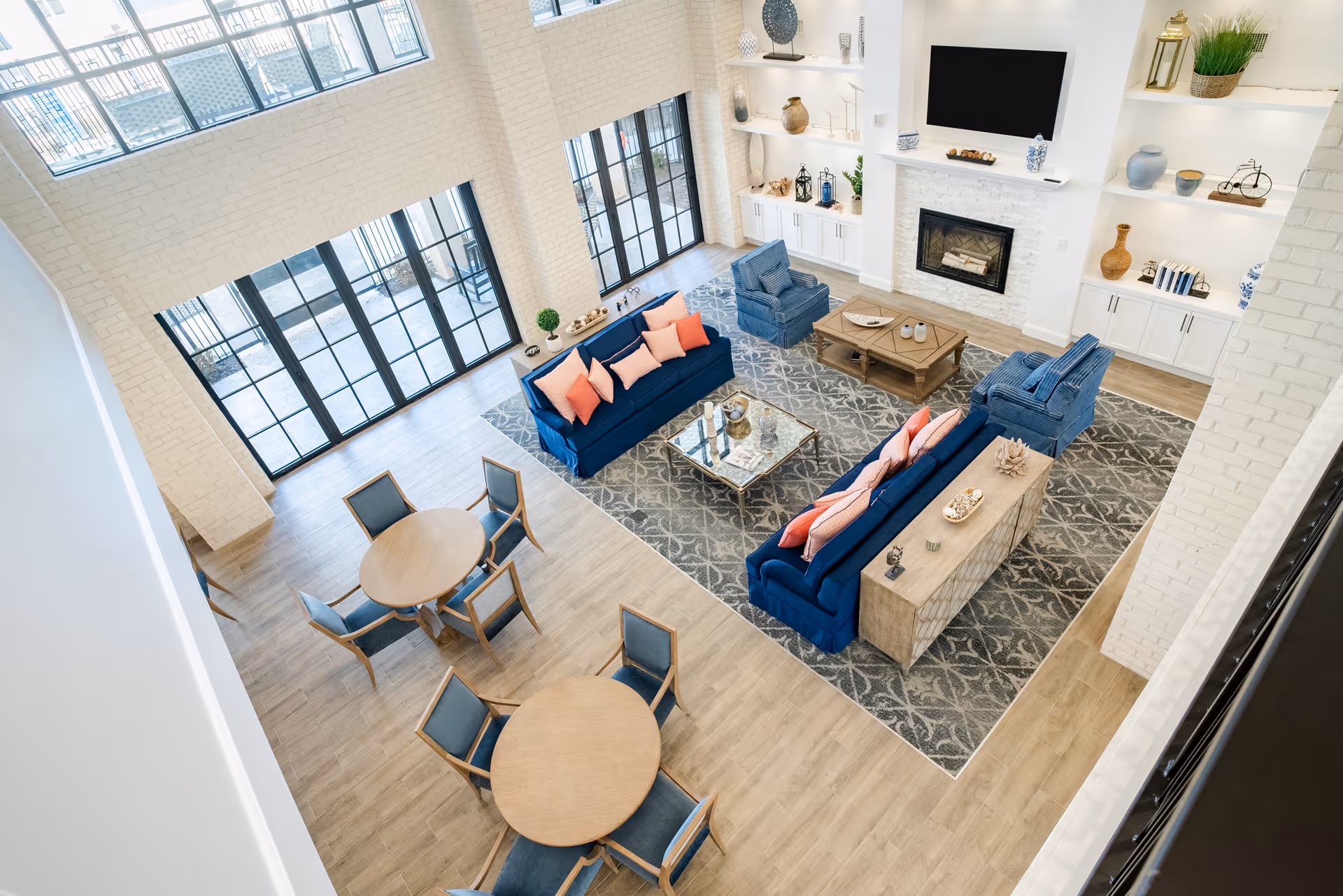 Bright, spacious senior living lounge with blue sofas, tables, fireplace, and large windows.