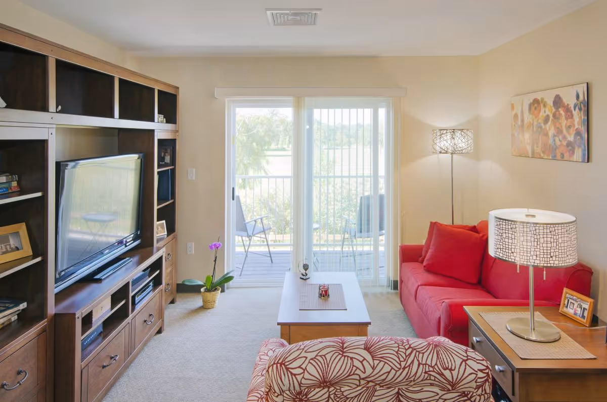 Bright living room with red sofa, coffee table, TV cabinet, and sliding balcony doors.