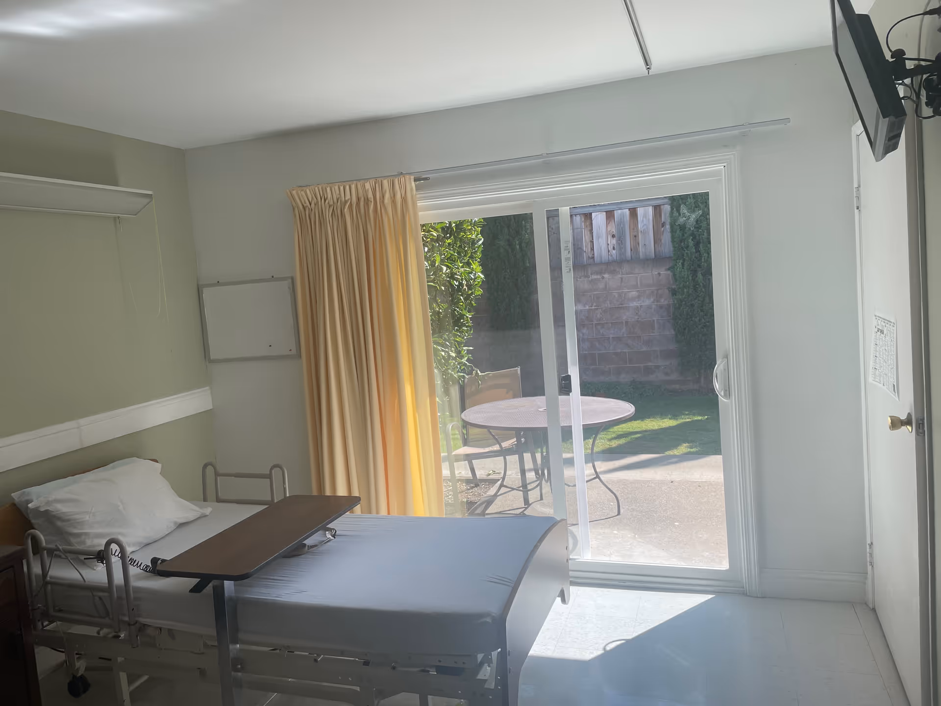 Hospital-style patient room featuring a bed, curtain, and sliding glass door to a patio.