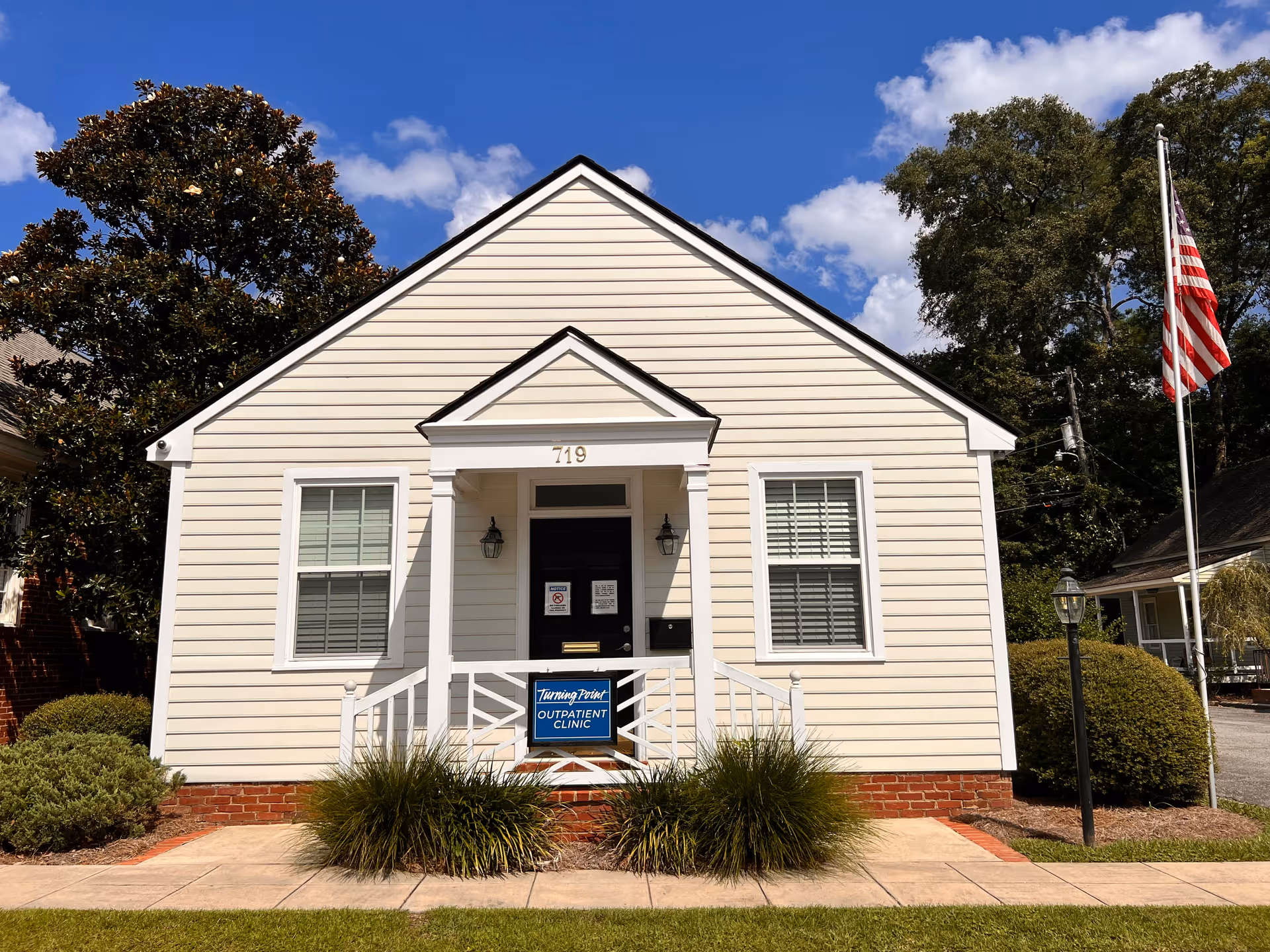 Small light-colored building with a front porch, steps, flagpole, and Turning Point Outpatient Clinic sign.