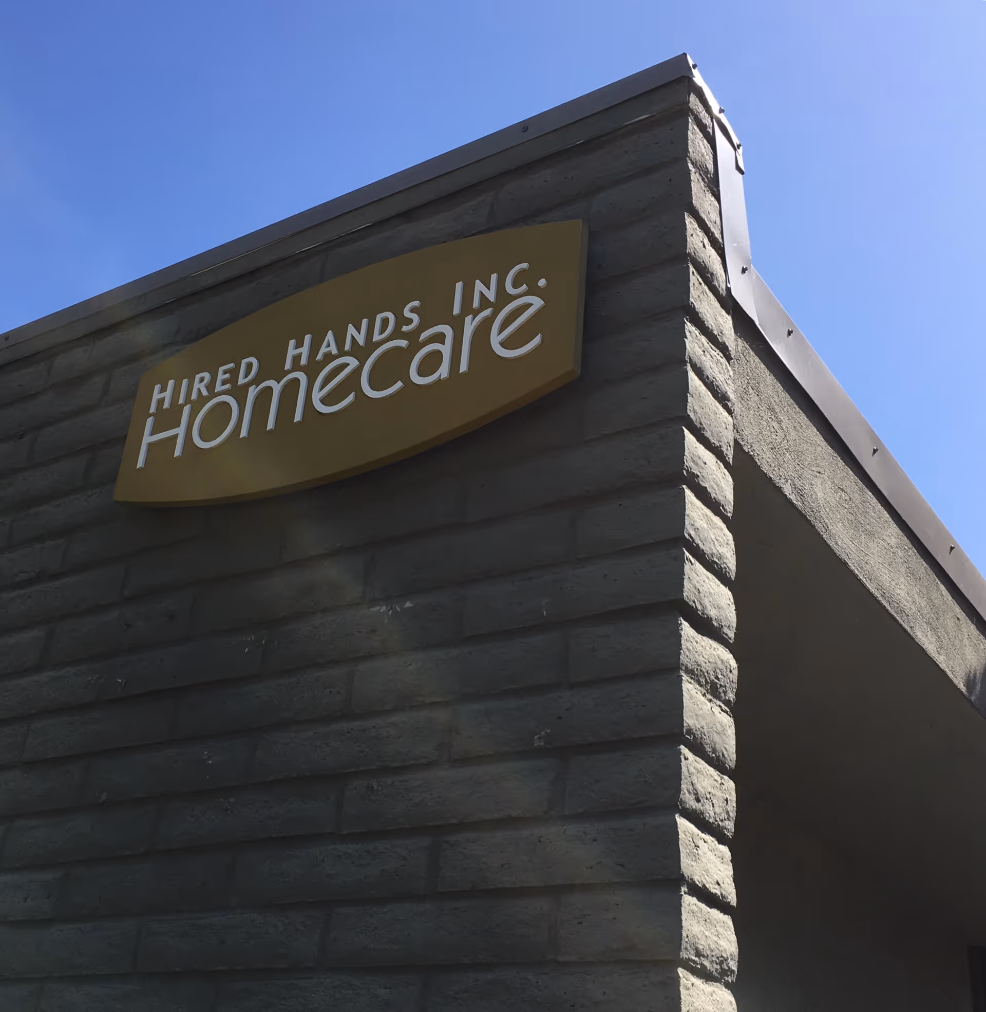 Exterior view of Hired Hands Homecare sign on building corner against blue sky.