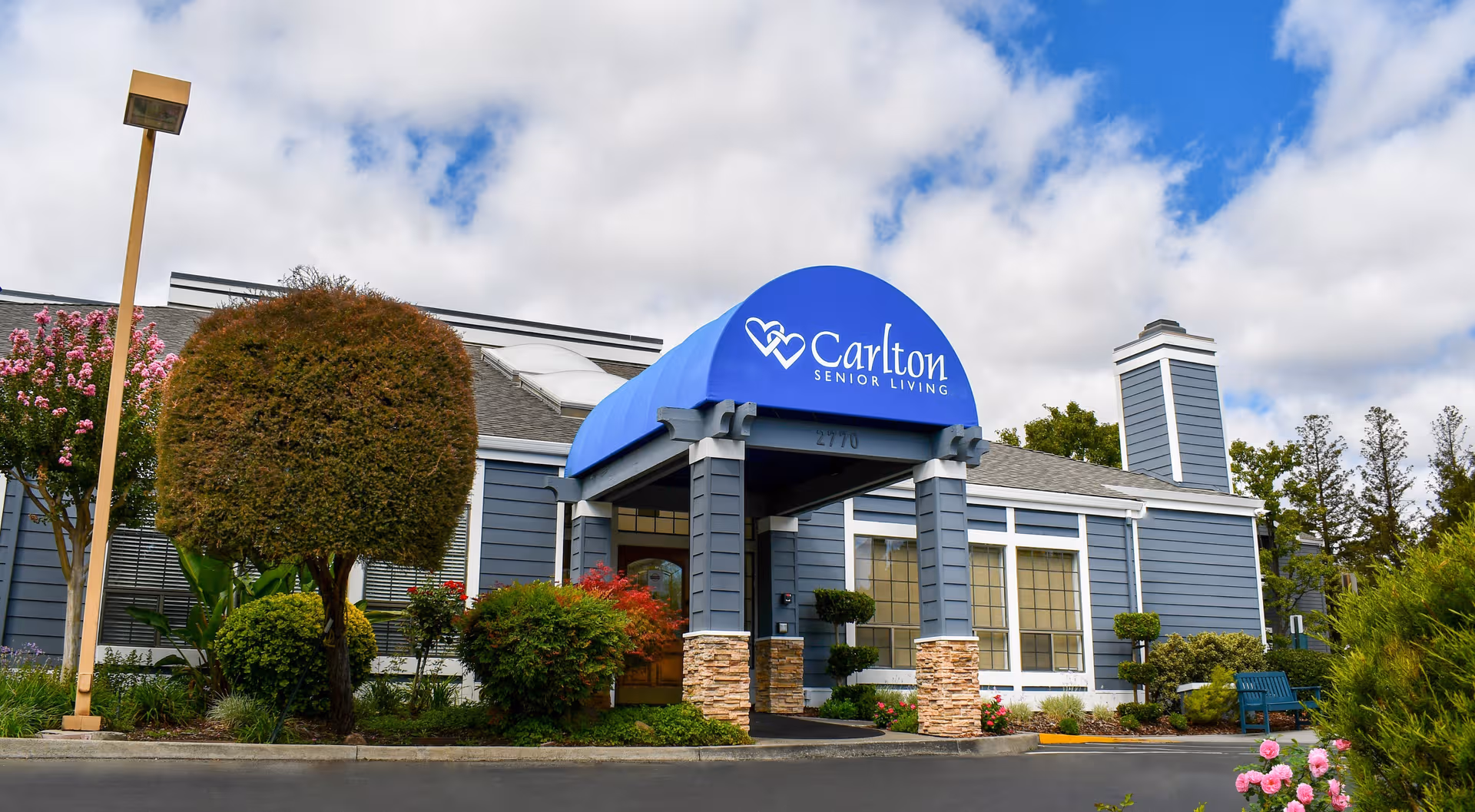Blue Carlton Senior Living entrance with an arched awning and manicured landscaping.