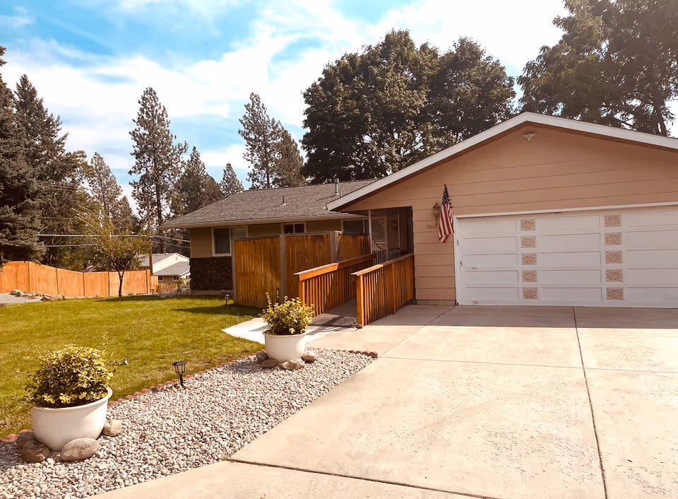 Single-story house with a wooden ramp, garage, flag, and front yard on a sunny day.