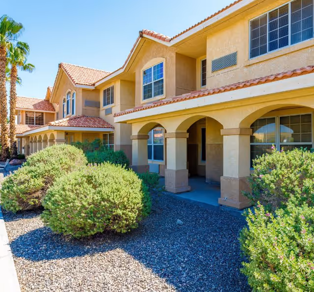 Exterior view of a beige senior living facility with arches and desert landscaping.