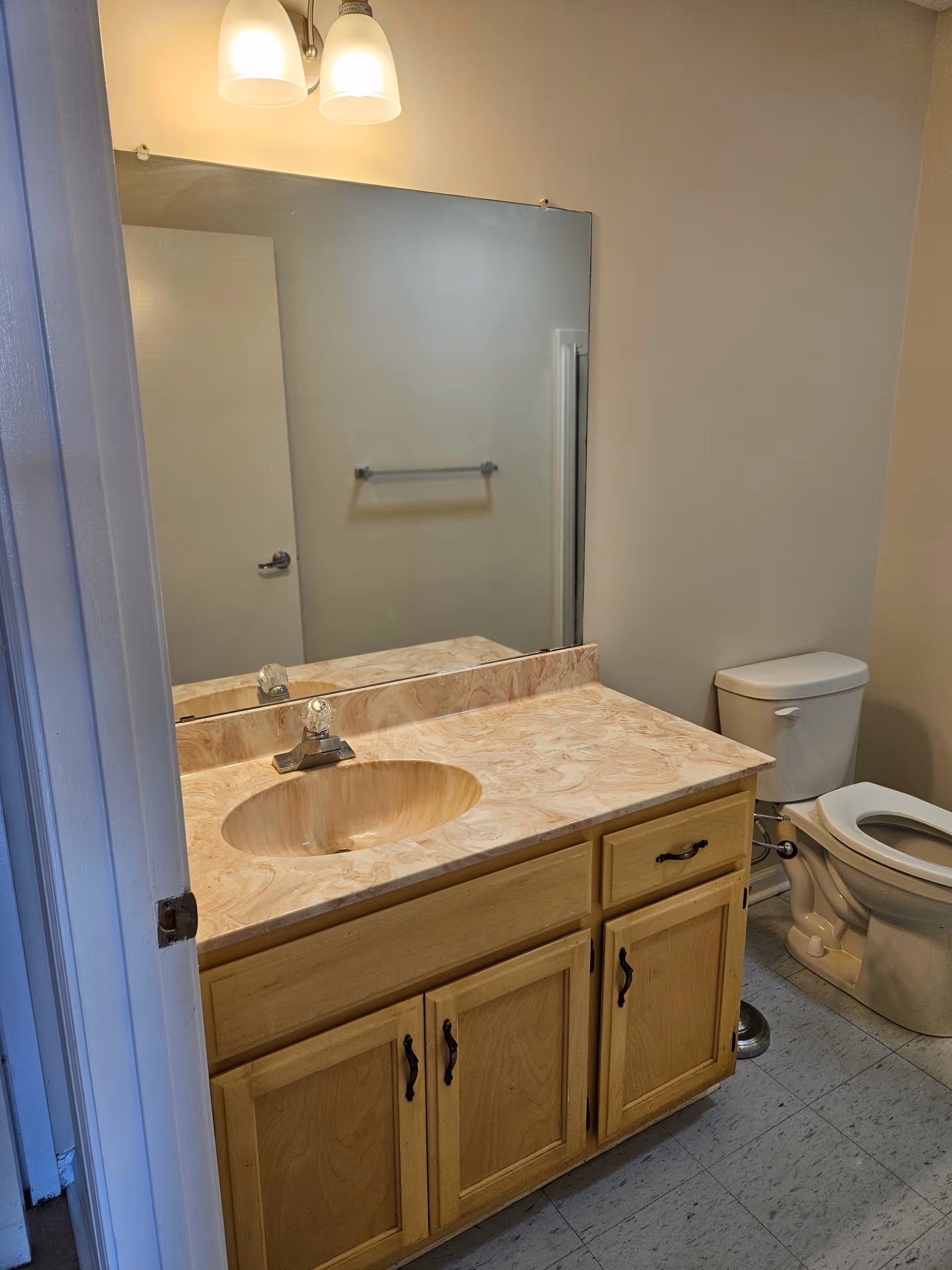 Bathroom with marble countertop sink, mirror, towel bar, and toilet in a senior facility.