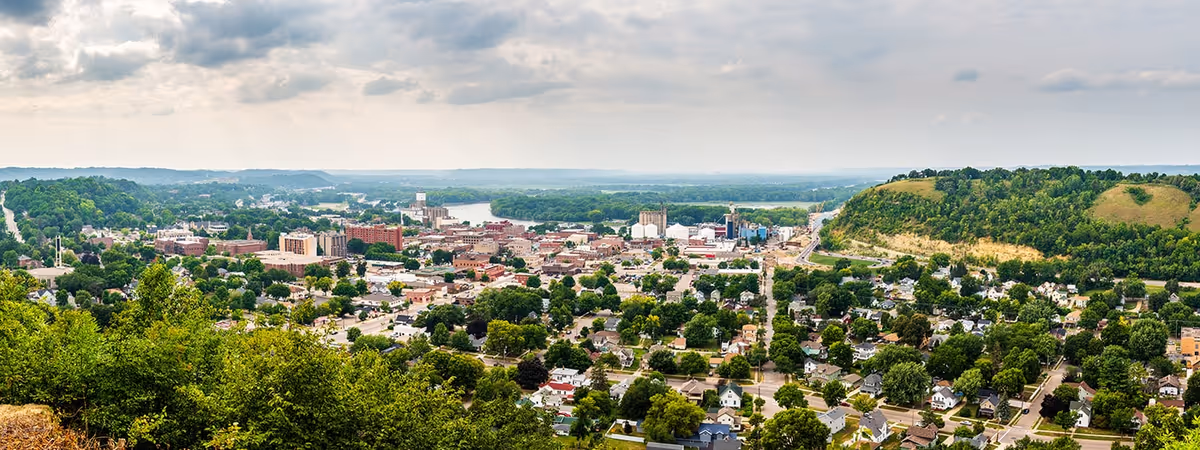 Panoramic view of Red Wing downtown from a hillside, with trees and distant river.