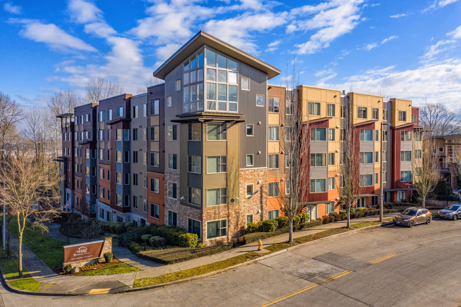 Colorful multi-story senior living building with a curved central tower, along a street, with parked cars.