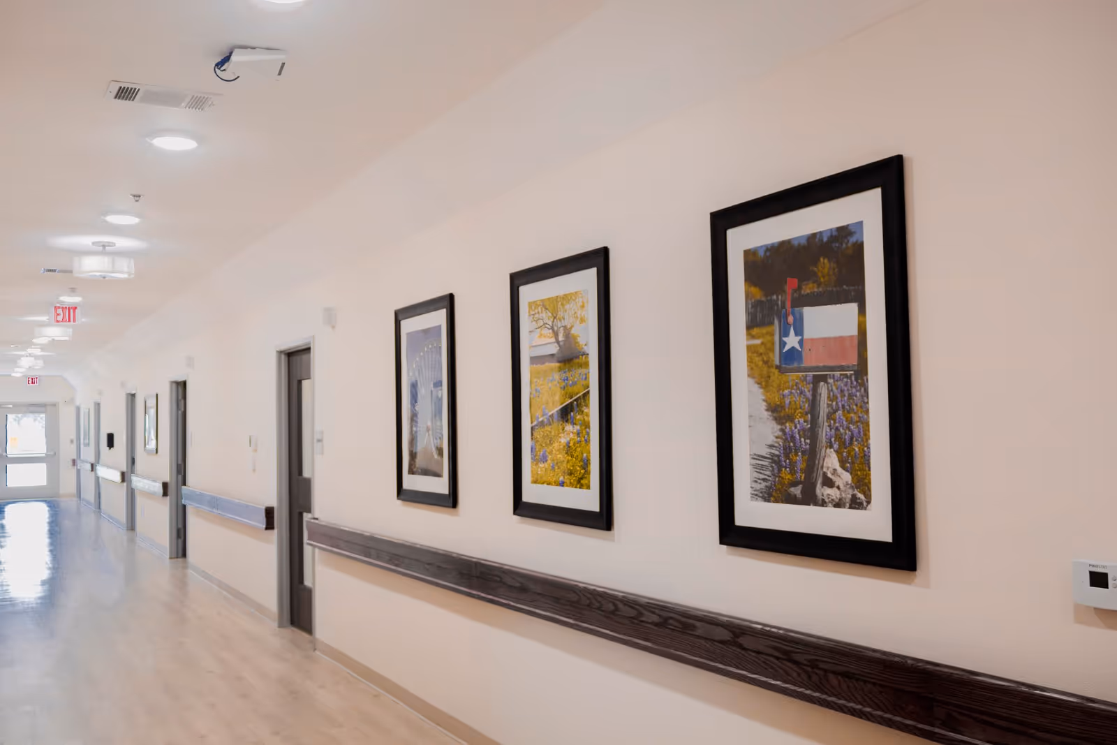 A long hallway with three framed pictures along a beige wall.