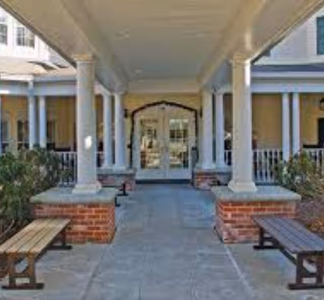 Front entrance of a senior living facility with columns, benches, and a paved walkway.