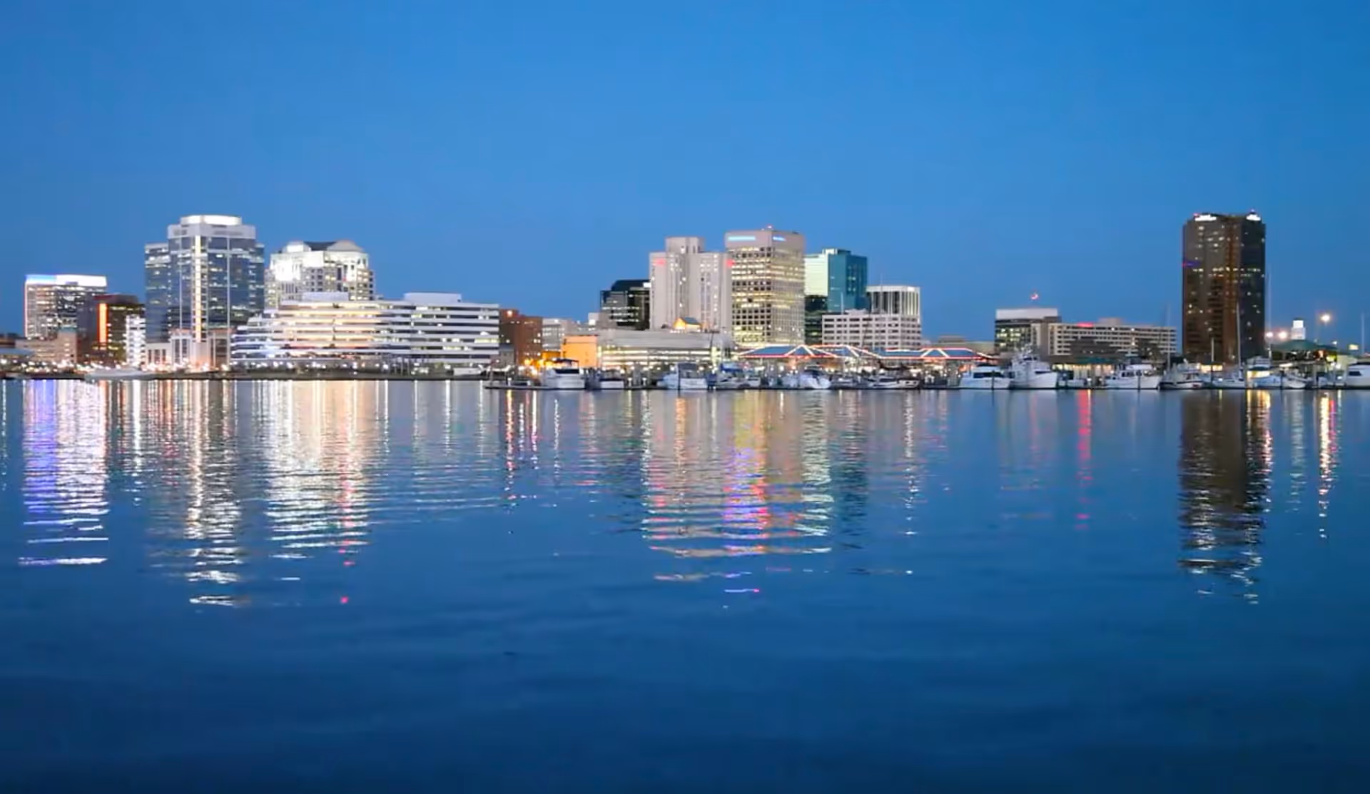Evening city skyline across calm water with brightly lit buildings along the shore.