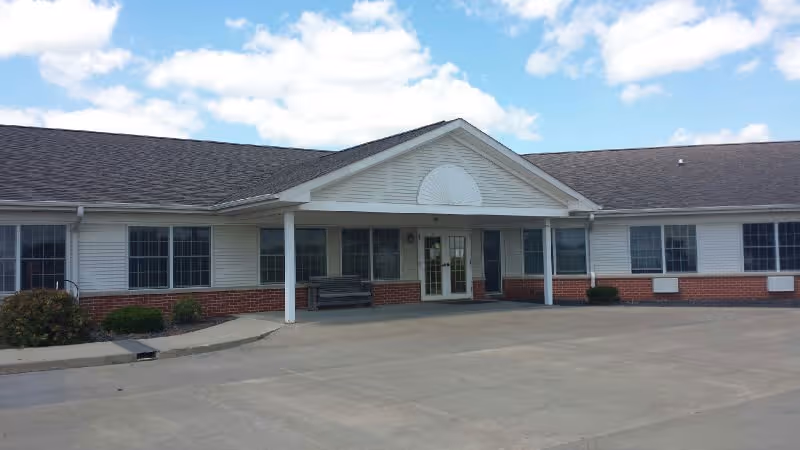 Single-story senior living facility exterior with white siding, brick base, and front entrance.