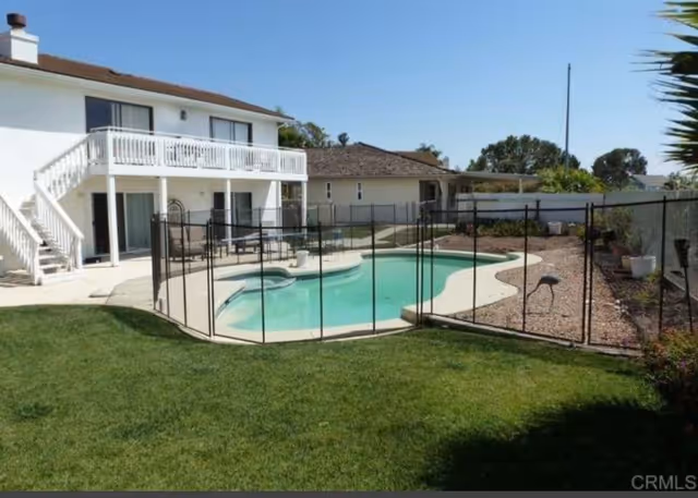 Fenced outdoor swimming pool area beside a two-story white building with lounge chairs.
