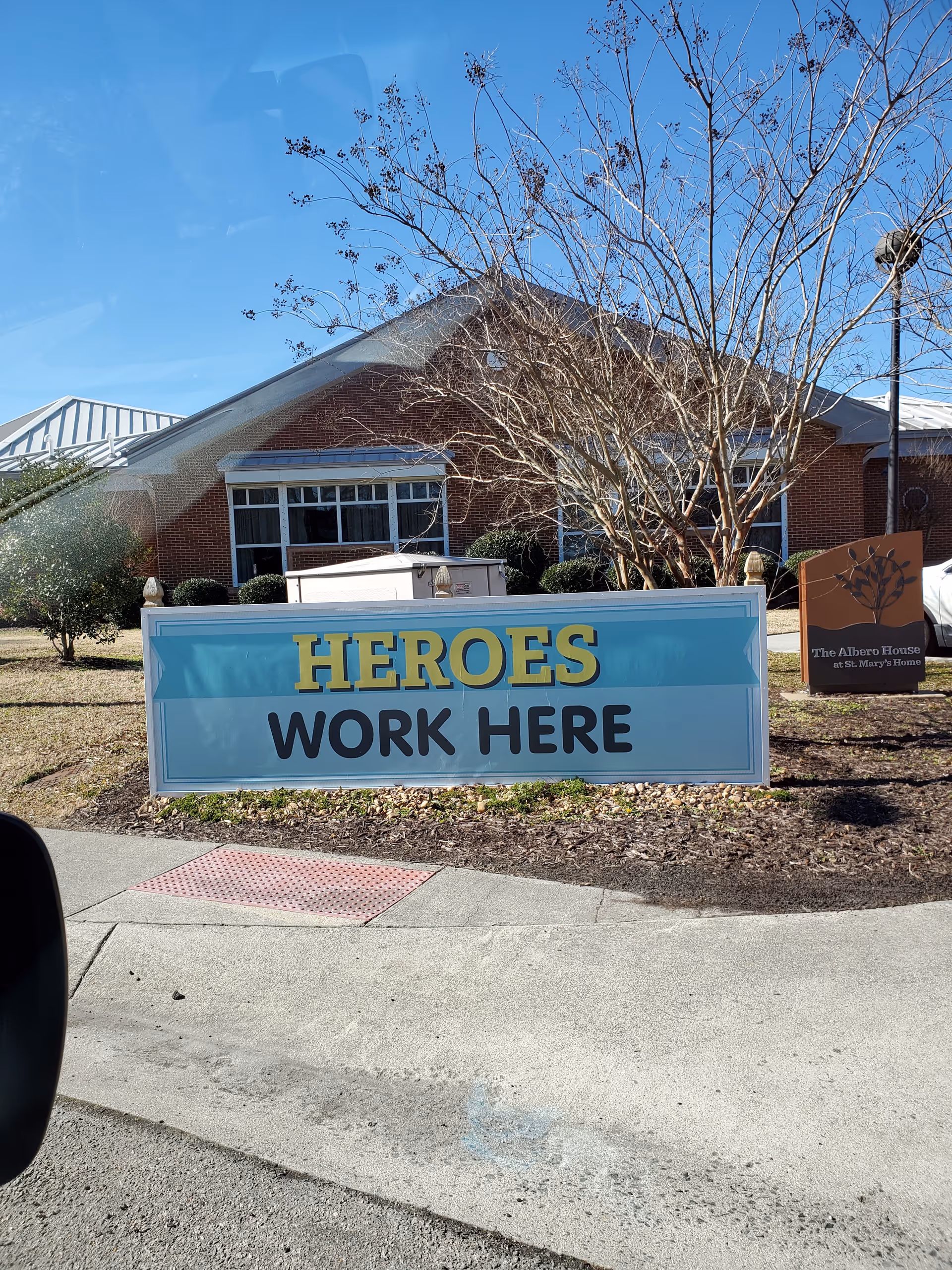 Exterior of a brick senior living home with a blue 'Heroes Work Here' sign.