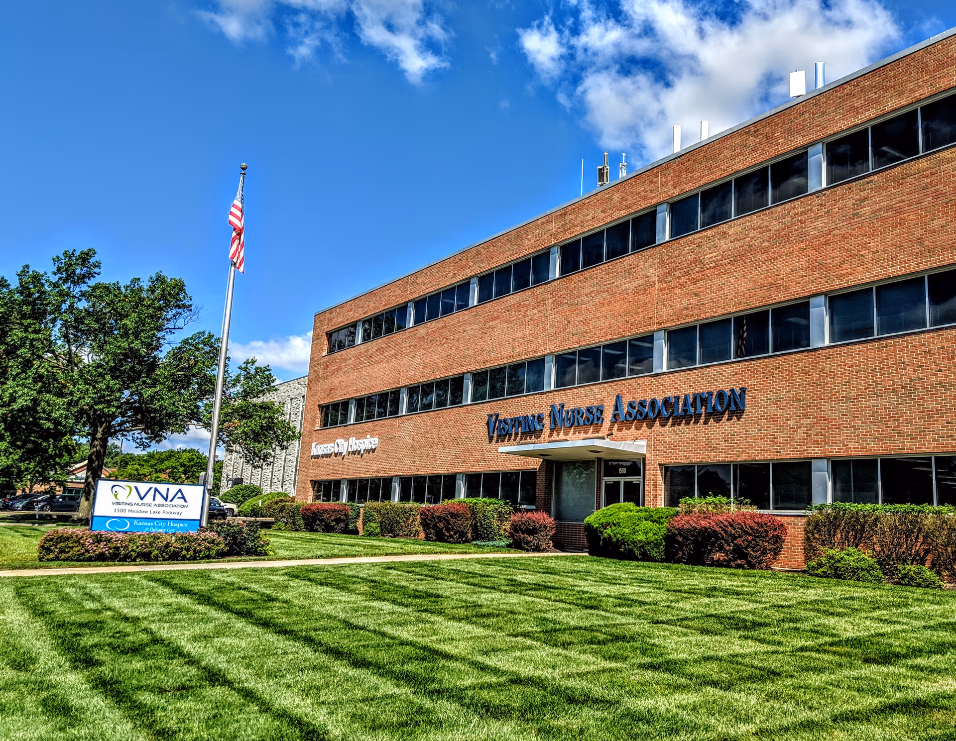 Brick three-story Visiting Nurse Association building with manicured lawn and flagpole.