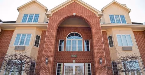 Brick-faced multi-story senior living building front with an arched entryway and multiple windows.