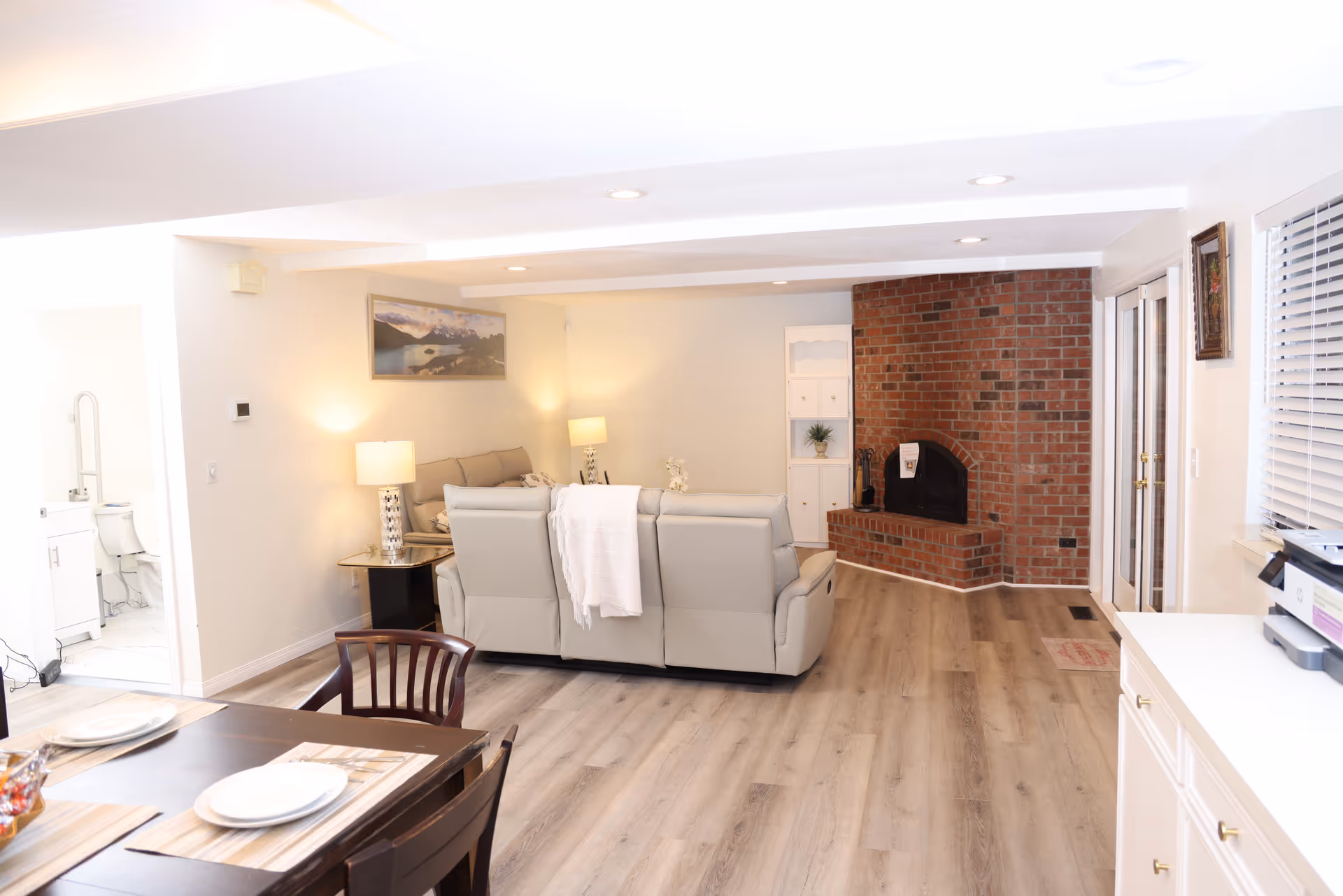 Bright communal living area with brick fireplace, beige seating, and dining table.