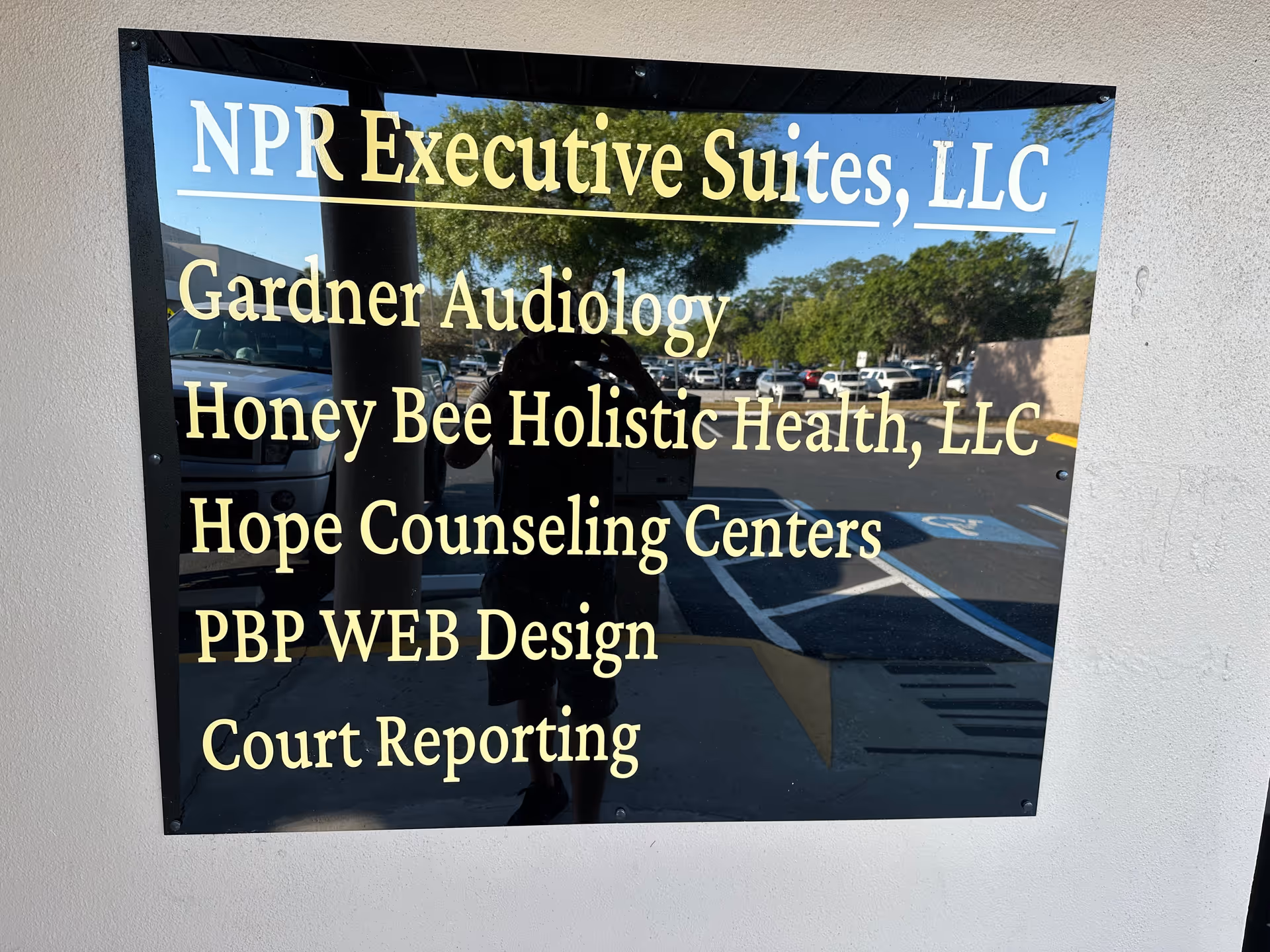 Reflective exterior wall sign listing multiple business names, including Honey Bee Holistic Health.