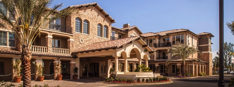 Exterior view of a Mediterranean-style senior living facility entrance with arches and palm trees.