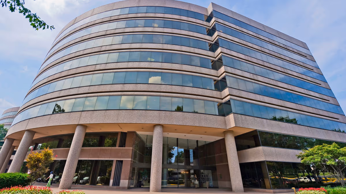 Modern curved-glass office building with tall concrete columns at the glass entrance.