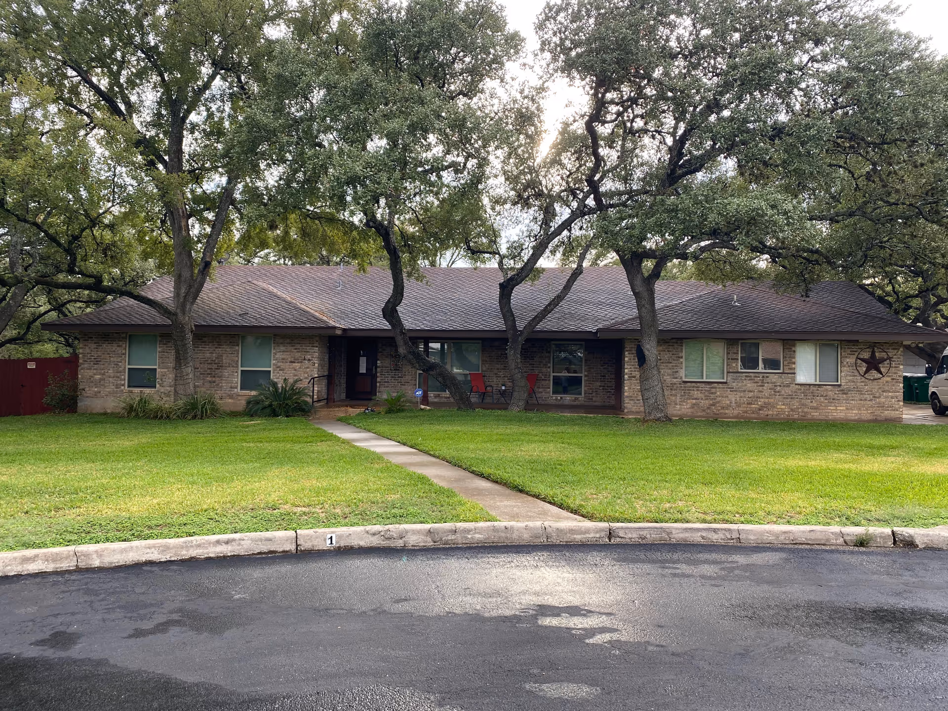 Single-story brick building with a front lawn, sidewalk, and large oak trees in front.