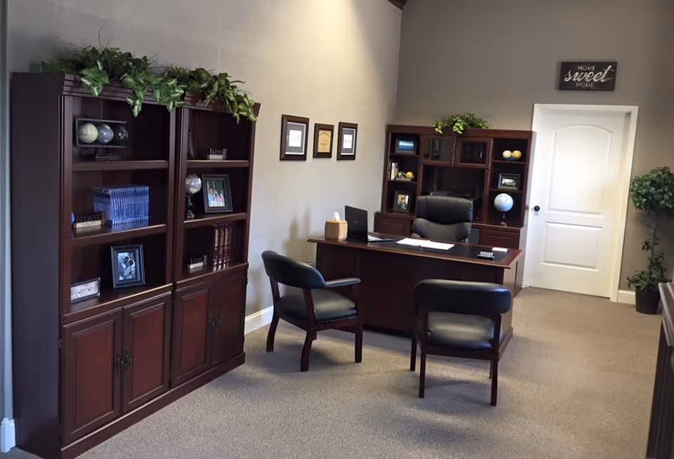 Reception area featuring a wooden desk, chairs, tall bookcases, and potted plants.