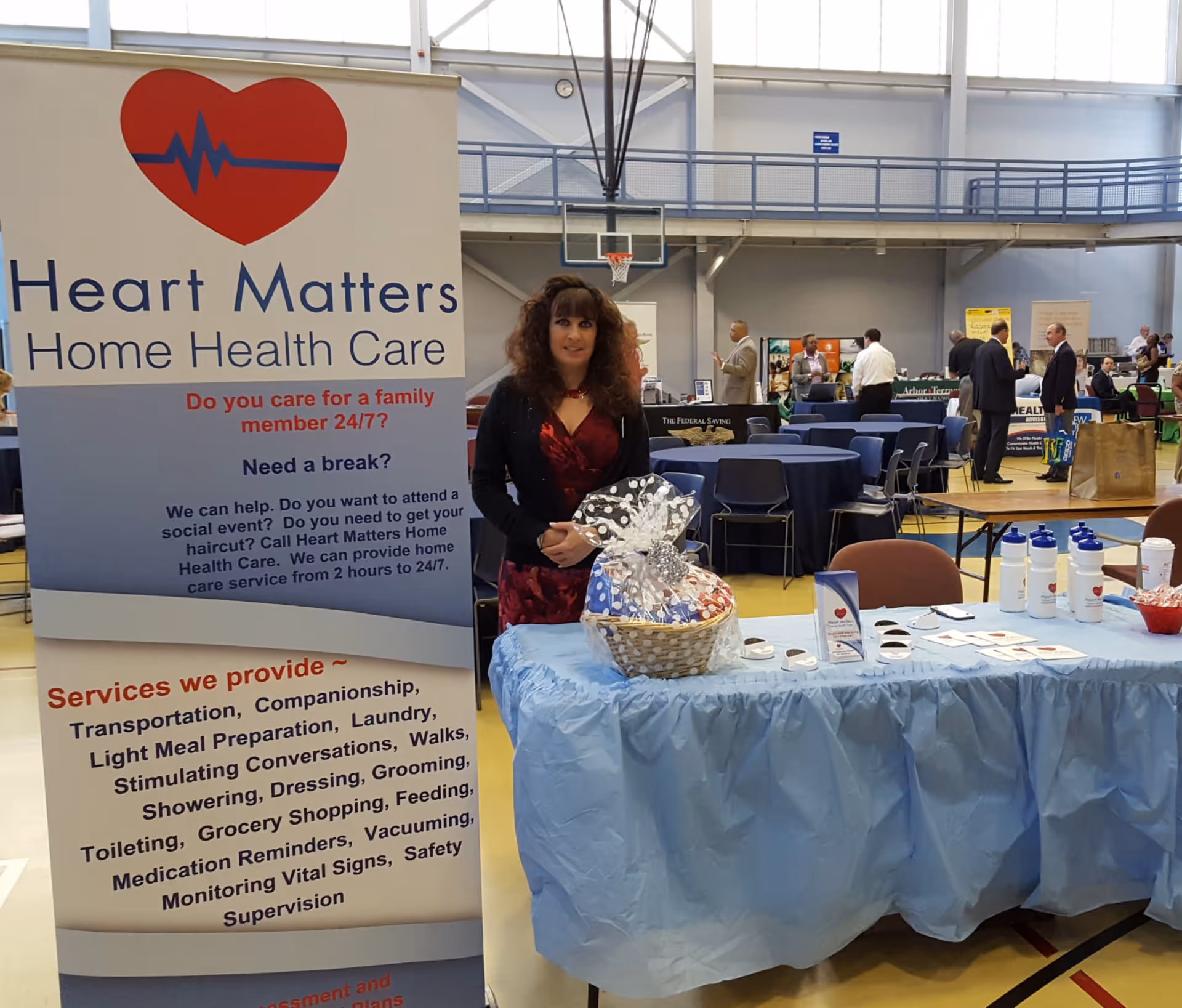 A woman stands beside a Heart Matters Home Health Care booth at a health fair.