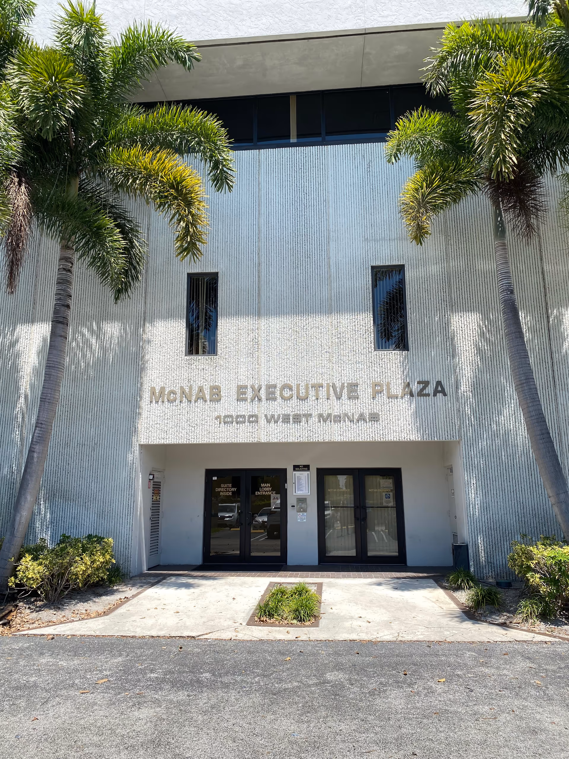 Exterior view of a modern building entrance with palm trees flanking doors.
