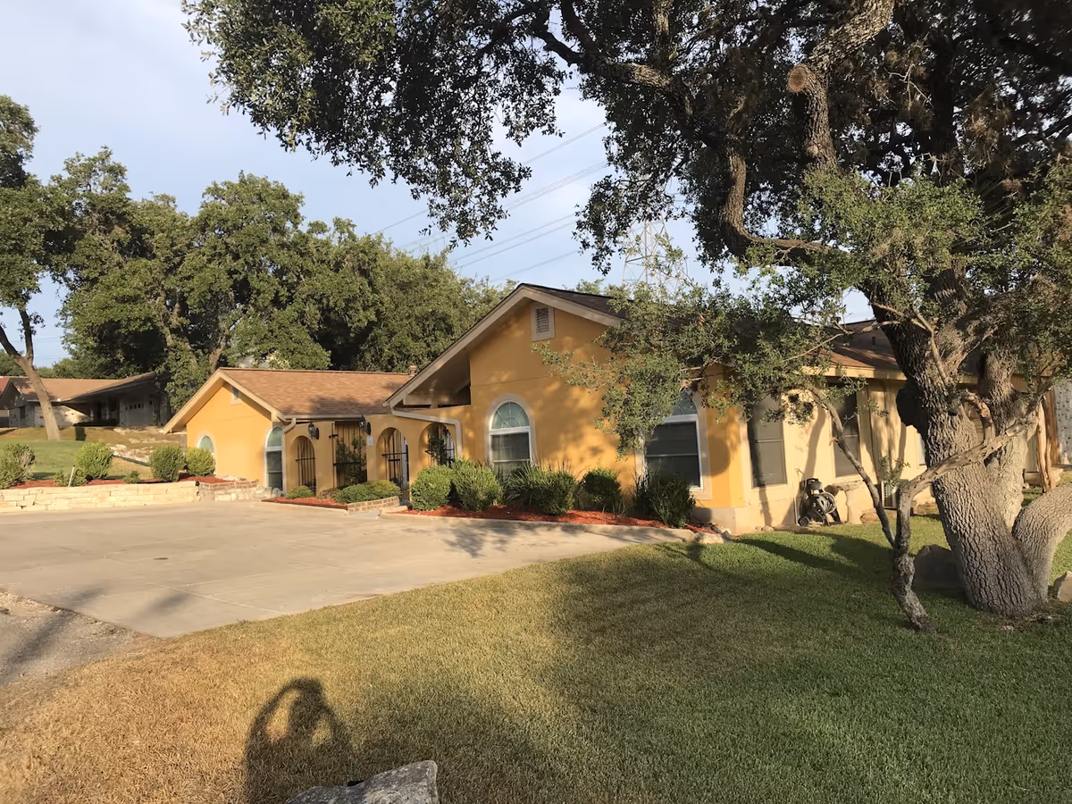 Exterior view of a yellow senior living facility with arched windows and trees.
