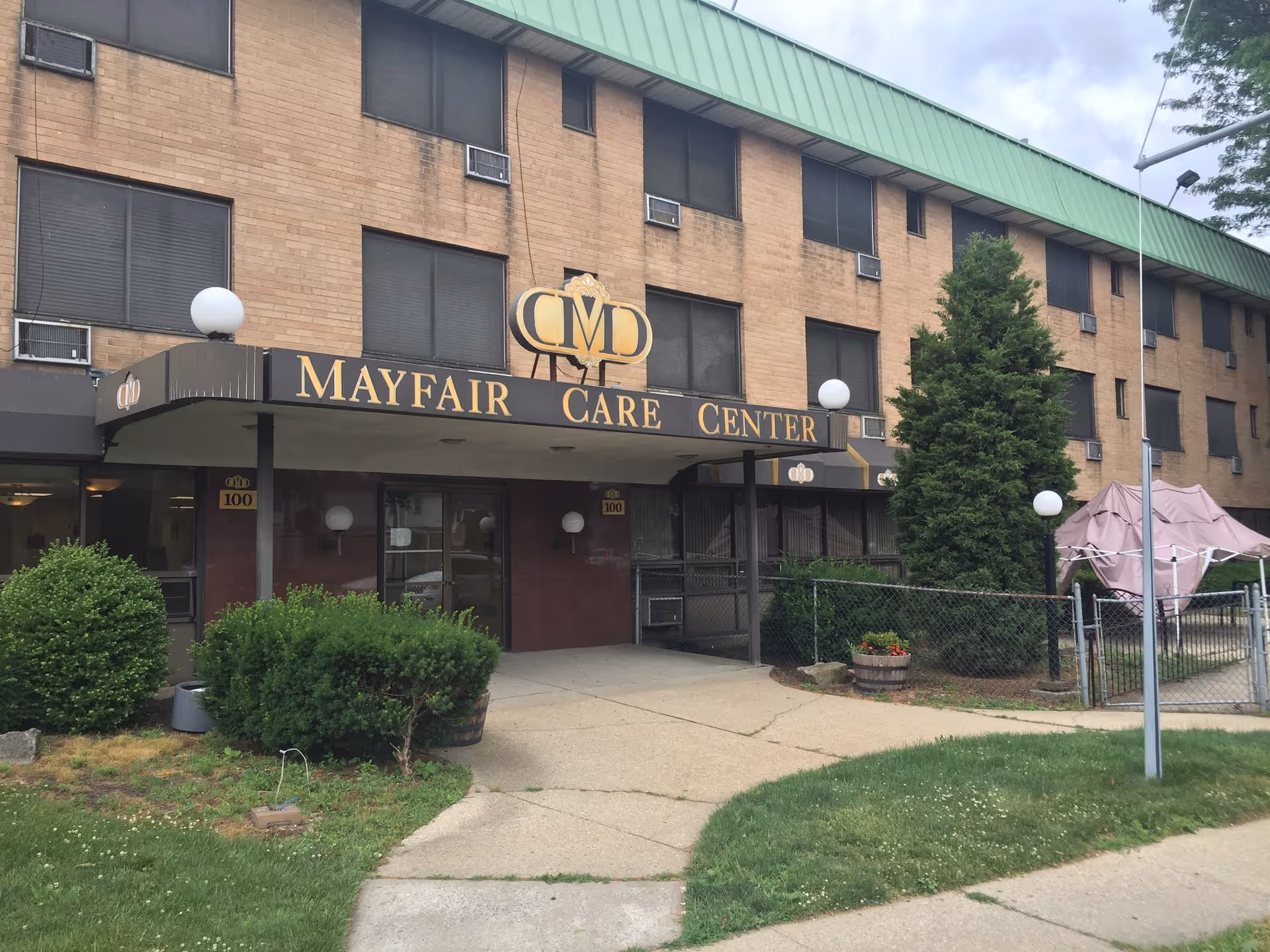Exterior view of Mayfair Care Center front entrance, brick building, and surrounding greenery.