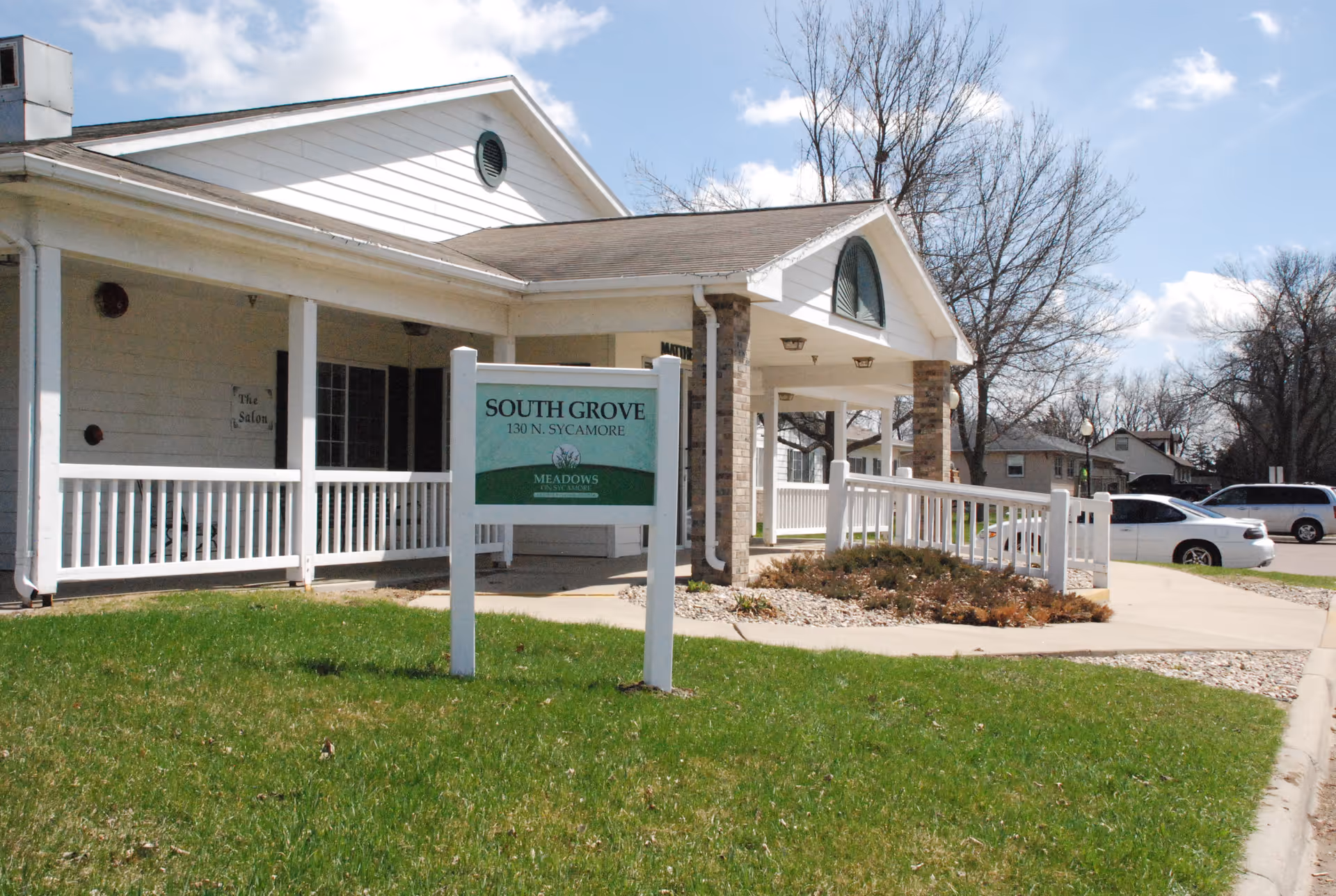 White, single-story senior living facility with a ramp and sign in front lawn.