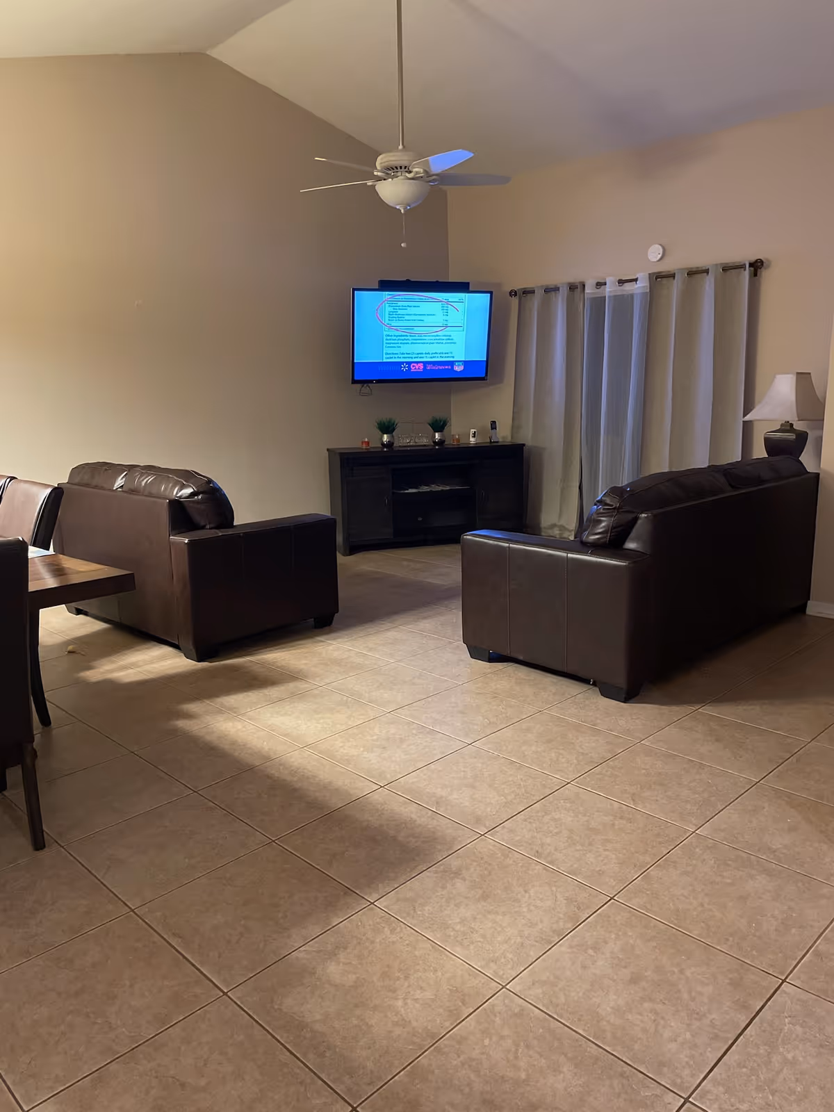 Living room with leather sofas, wall-mounted TV, ceiling fan, and curtains.