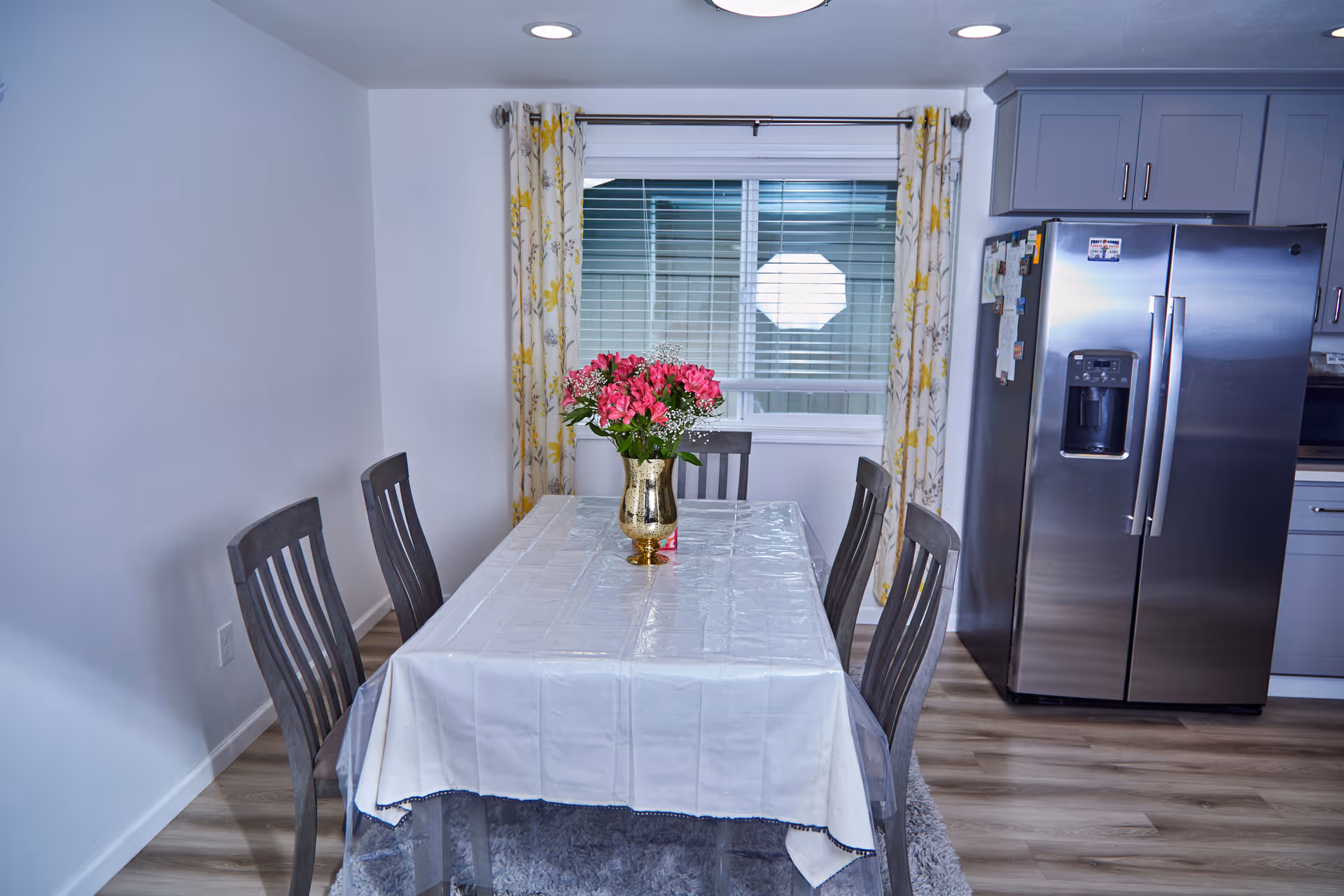 Dining room with a table, chairs, flowers, window, and a stainless refrigerator.