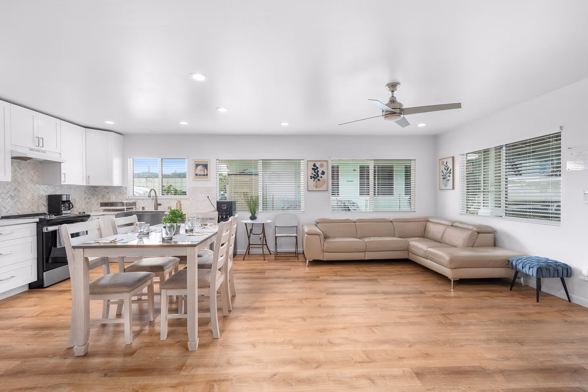 Bright open living area with beige sectional sofa, dining table, and white kitchen cabinets.