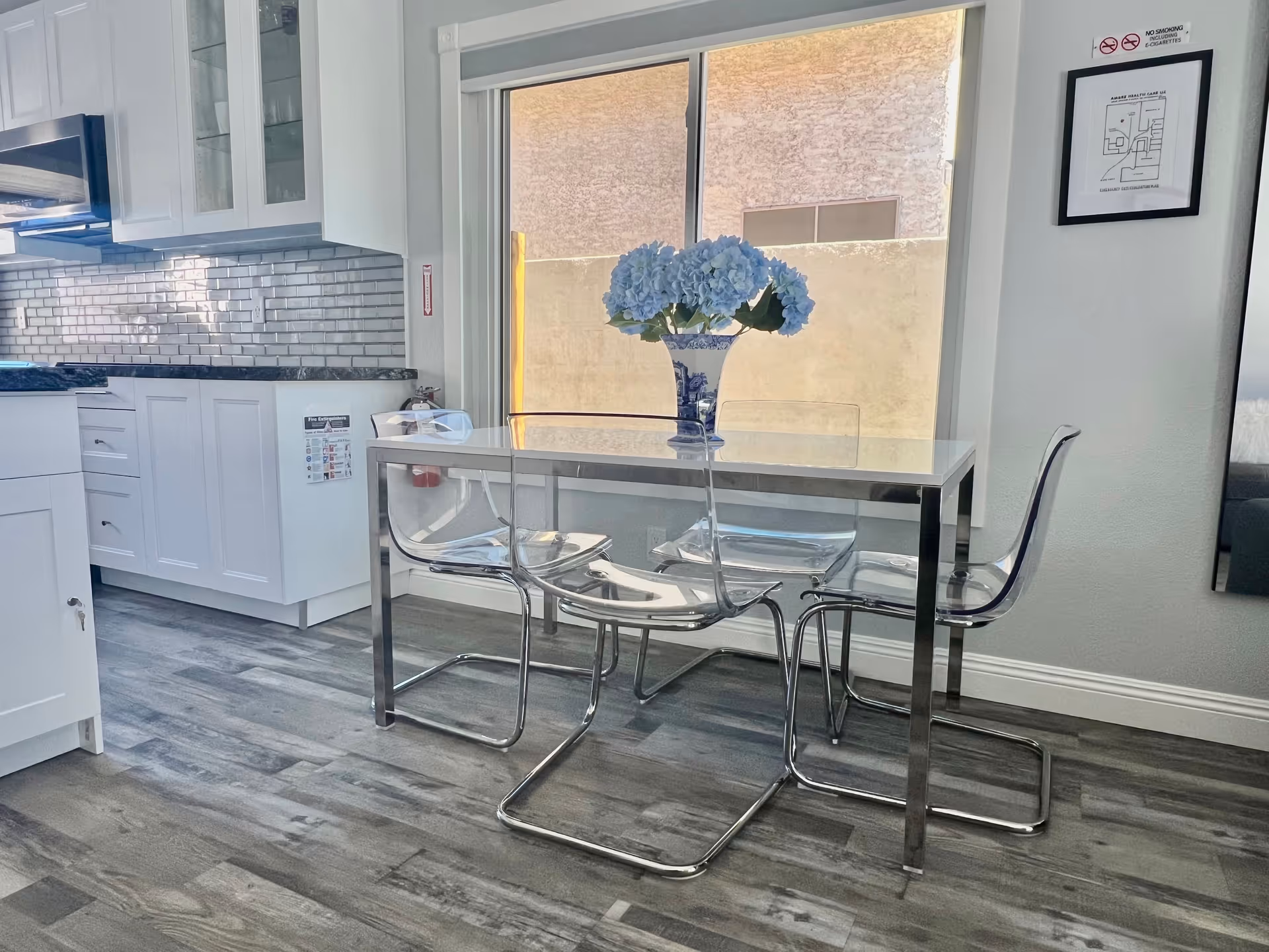 Modern kitchen and dining area with glass table, clear chairs, and blue hydrangea centerpiece.
