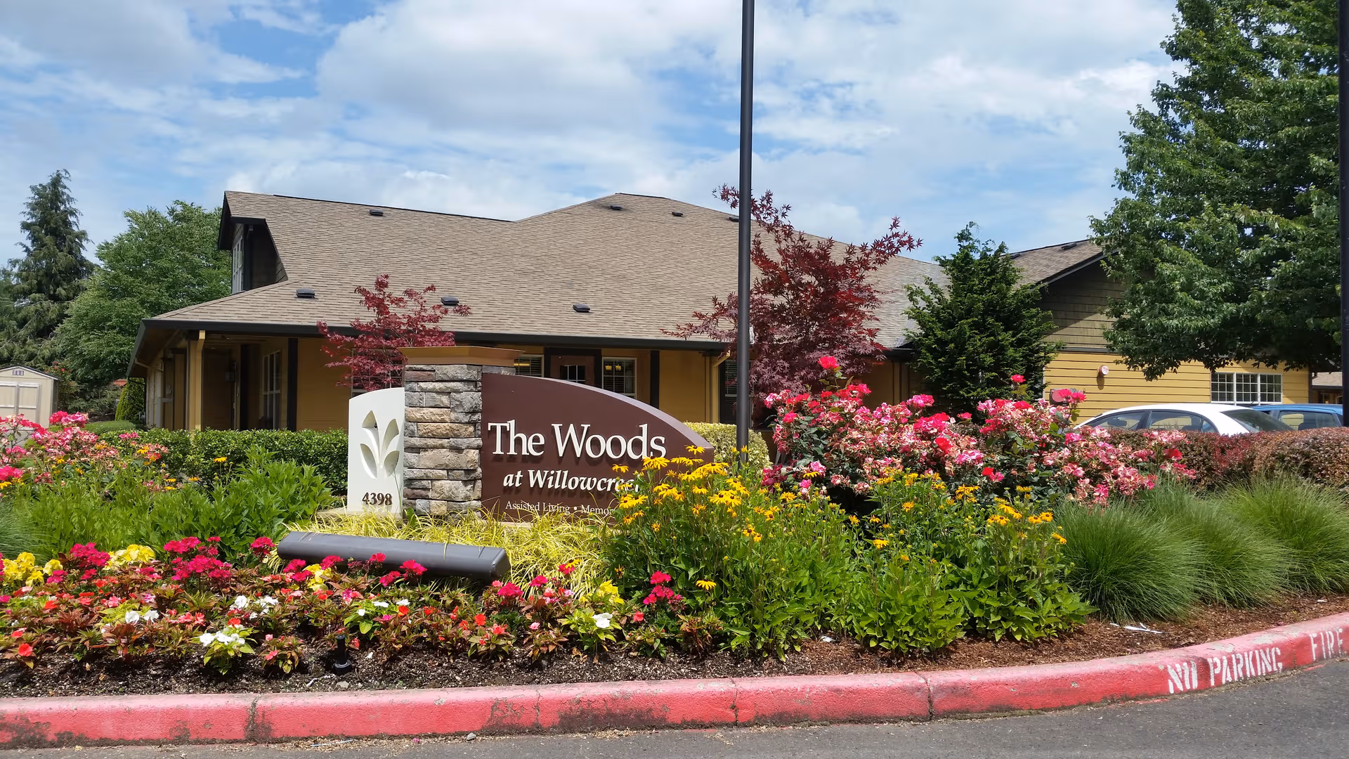 Exterior view of a senior living facility with a landscaped flower bed and sign.