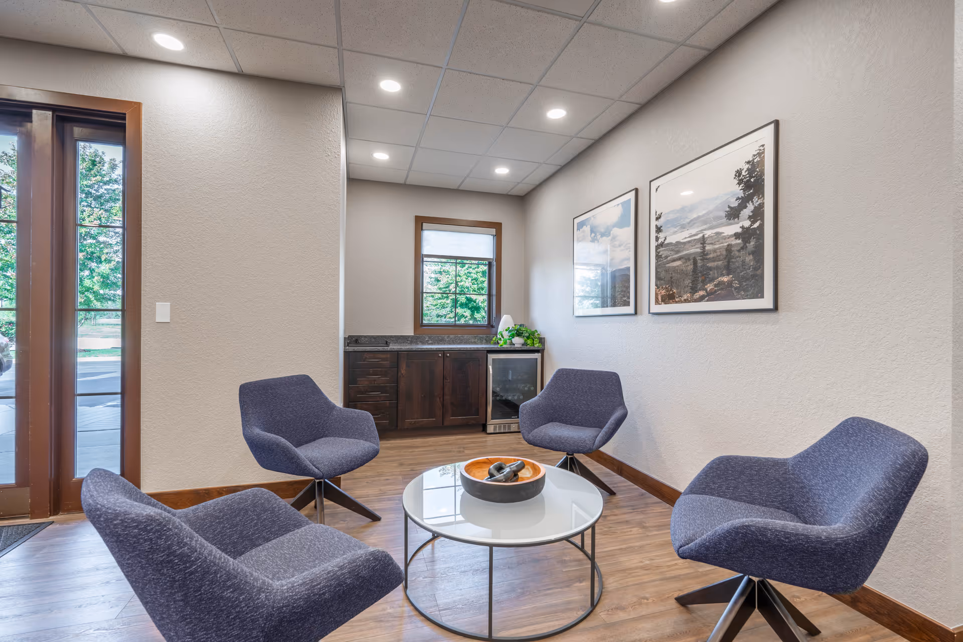 A modern waiting lounge with four blue chairs around a circular glass coffee table.