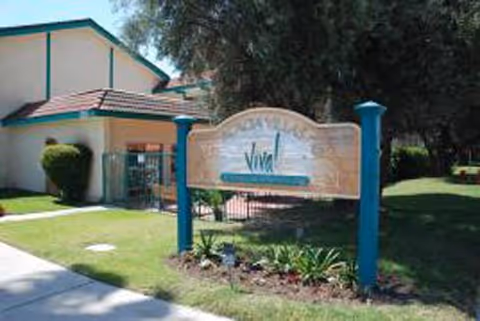 Exterior view of a senior living facility with a decorative sign and landscaping.
