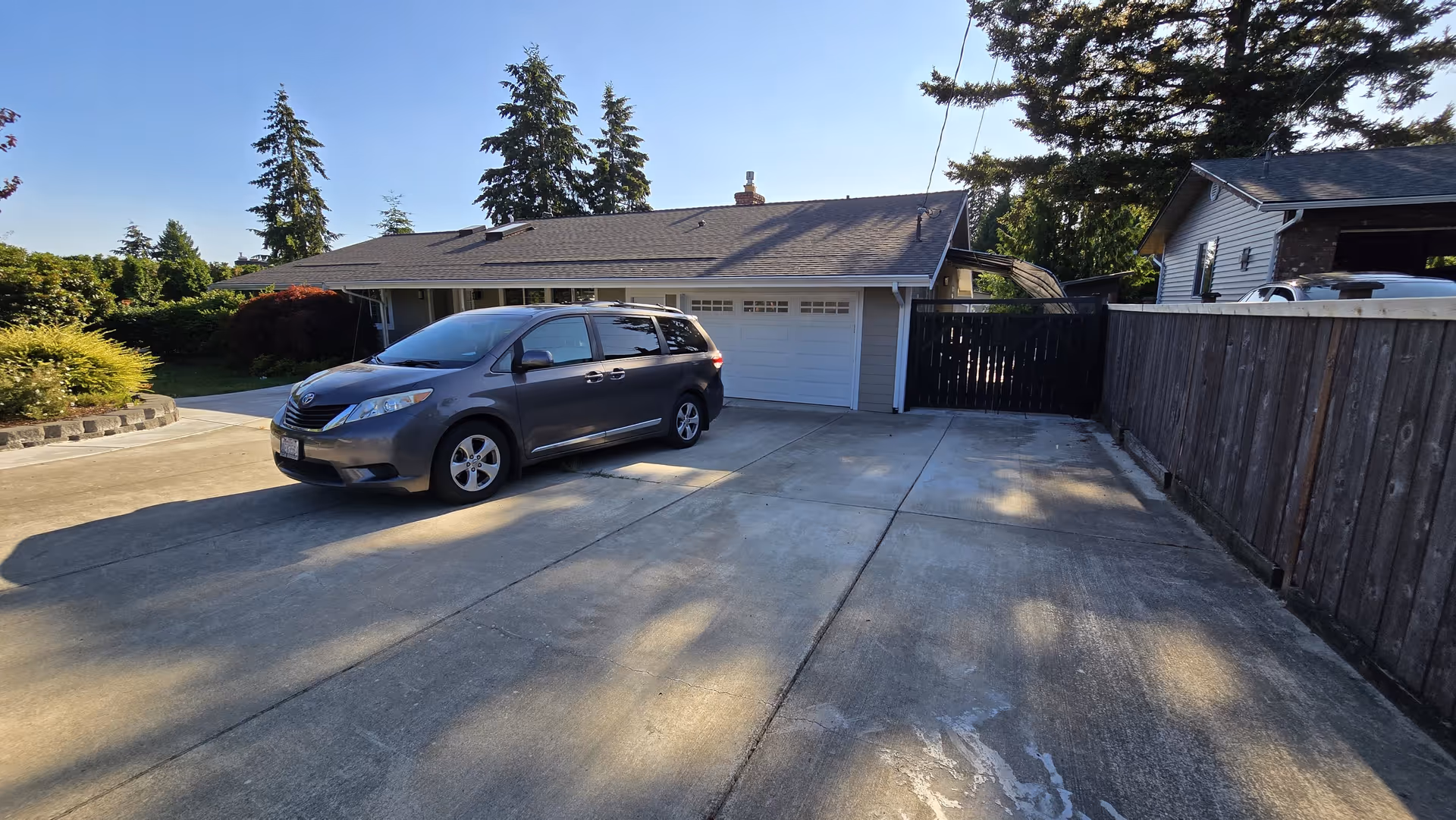Residential single-story house with attached double garage, gray minivan, and wooden fence.