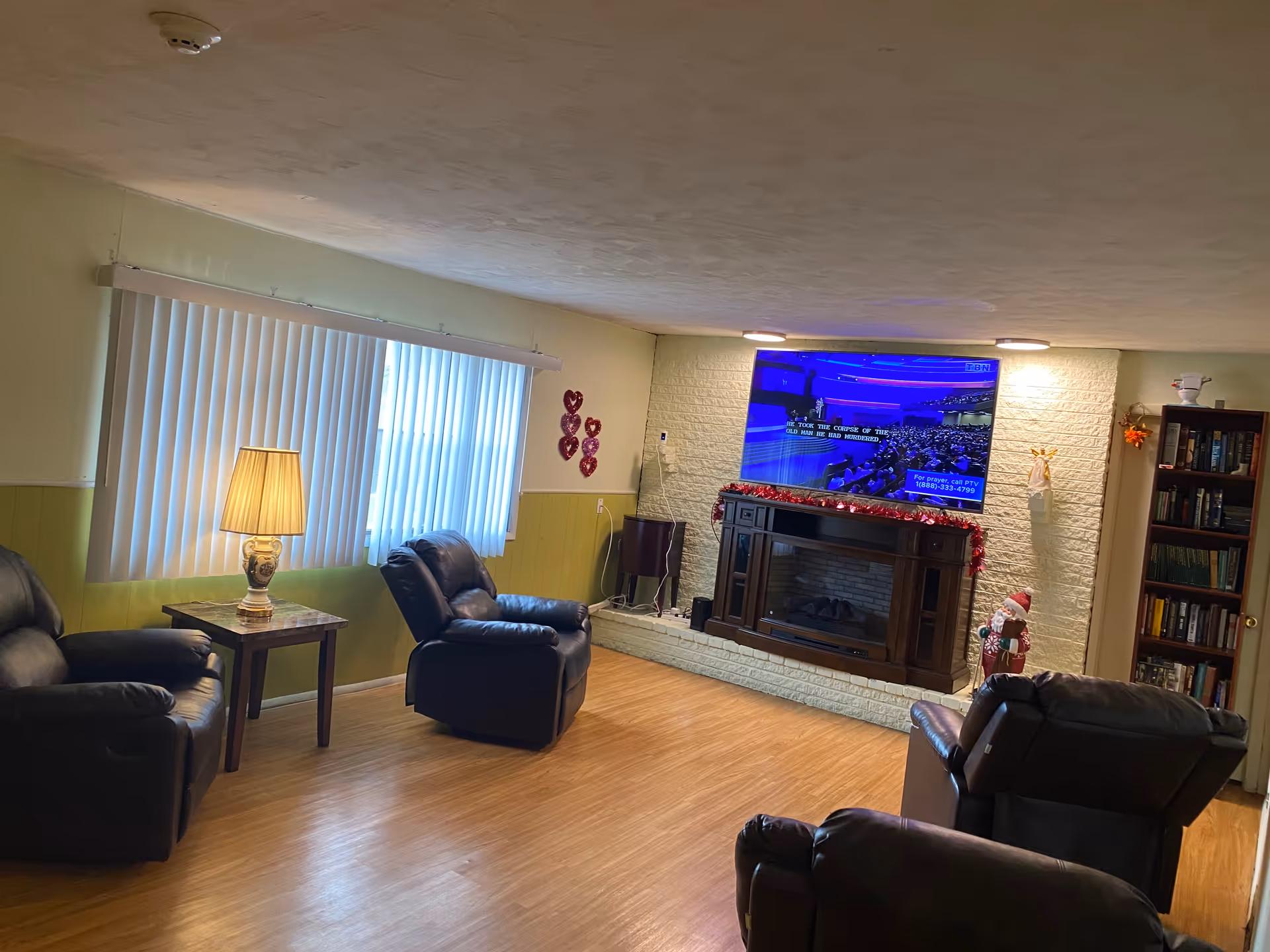 Leather recliners and a sofa surround a brick fireplace with a large TV.